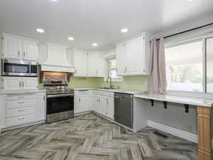 Remodeled Kitchen with stainless steel appliances, white cabinetry, recessed lighting, parquet floors, and light stone countertops