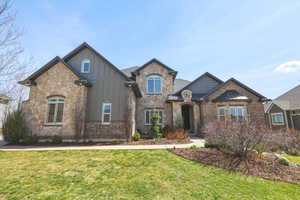 French country inspired facade with board and batten siding, a front lawn, brick siding, and stone siding