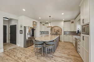 Kitchen with stainless steel appliances, a breakfast bar area, two tone color scheme, backsplash, and light stone counters
