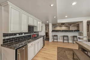 Kitchen with a kitchen bar, white cabinets, light wood-style floors, recessed lighting, and ornate columns