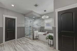 Bathroom featuring a wainscoted wall, a soaking tub, a shower stall, a decorative wall, and hanging lights