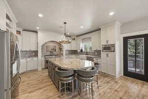 Two tone kitchen featuring stainless steel appliances, a kitchen bar, light stone countertops, light wood finished floors, and two tone cabinetry