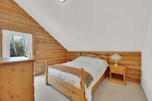 Bedroom featuring rustic walls, light carpet, and vaulted ceiling