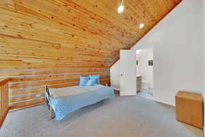 Bedroom with log walls, light colored carpet, a vaulted wooden ceiling, and ensuite bath