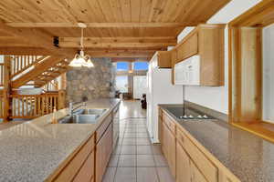 Kitchen featuring light wood finish cabinets, decorative light fixtures, a wood ceiling with exposed beams, white appliances, and light tile patterned floors