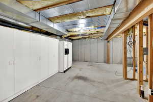 Unfinished basement with white fridge with ice dispenser