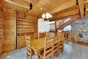 Dining room with a chandelier, light tile patterned flooring, and a wood ceiling with exposed beams