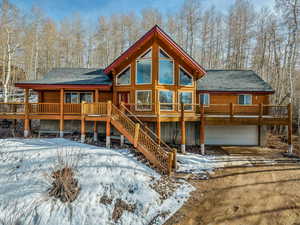 Snow covered back of property with driveway, roof with shingles, a deck, and a garage