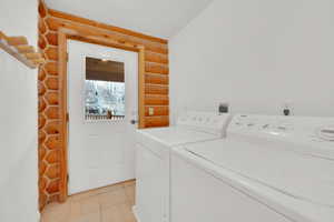 Laundry room with rustic walls, washer and dryer, and light tile patterned floors