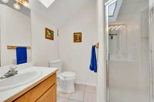 Bathroom featuring a skylight, vanity, a shower stall, light tile patterned floors, and lofted ceiling