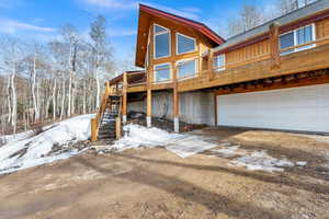 Snow covered back of property with a deck, an attached garage, and driveway