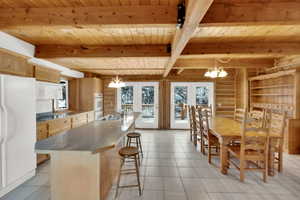 Kitchen with hanging lights, white appliances, healthy amount of natural light, and a wooden ceiling with exposed beams