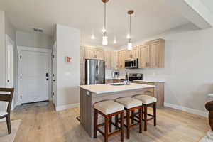 Kitchen featuring light wood finish cabinetry, stainless steel appliances, a kitchen breakfast bar, light wood-style floors, and a kitchen island with sink