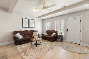 Living room featuring ceiling fan, light wood-style flooring, and beam ceiling