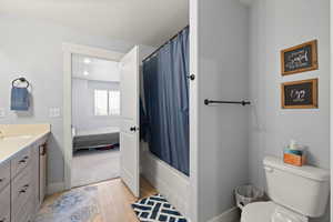 Full bath with vanity, light wood-type flooring, ensuite bath, shower / tub combo with curtain, and a textured ceiling