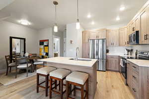 Kitchen with stainless steel appliances, light stone counters, an island with sink, light wood-type flooring, and a breakfast bar area