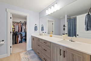 Bathroom with a shower with shower curtain, double vanity, light wood finished floors, a textured ceiling, and a spacious closet