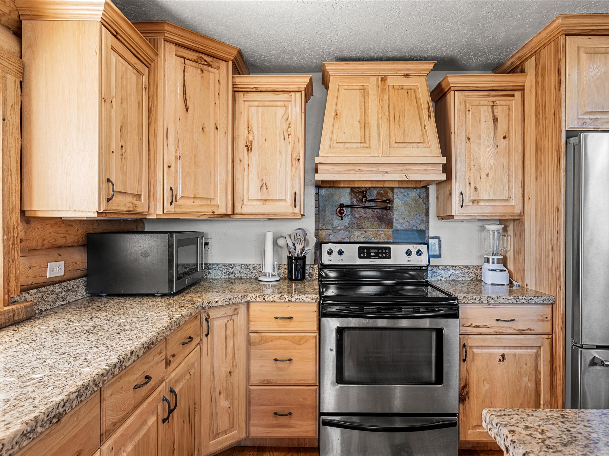 Kitchen with stainless steel appliances, light stone countertops, light wood finish cabinets, and a textured ceiling