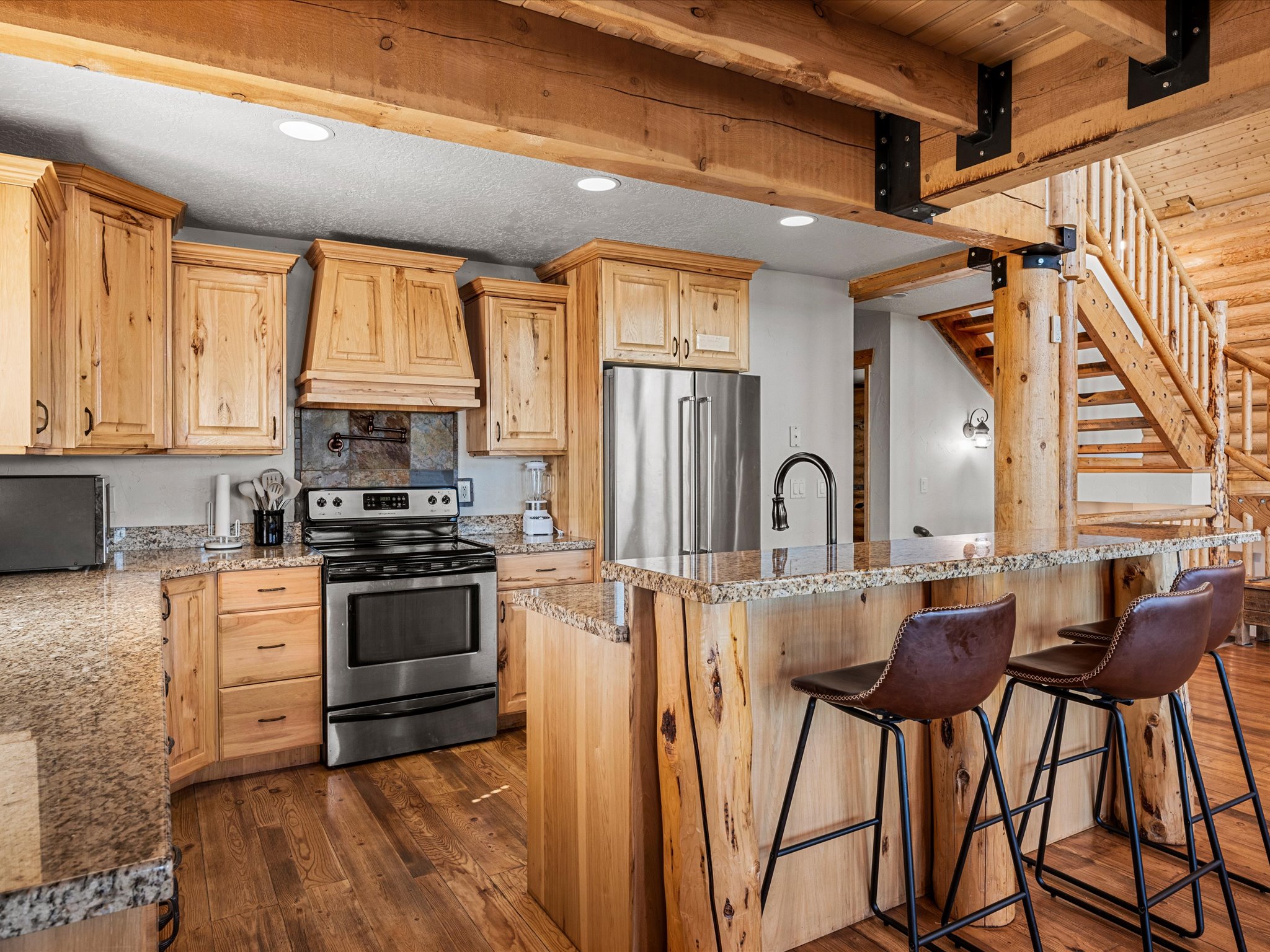Kitchen featuring light wood finish cabinetry, stainless steel appliances, dark wood-type flooring, a center island with sink, and light stone countertops