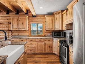 Kitchen featuring rustic walls, stainless steel appliances, dark wood finished floors, light wood finish cabinets, and beam ceiling