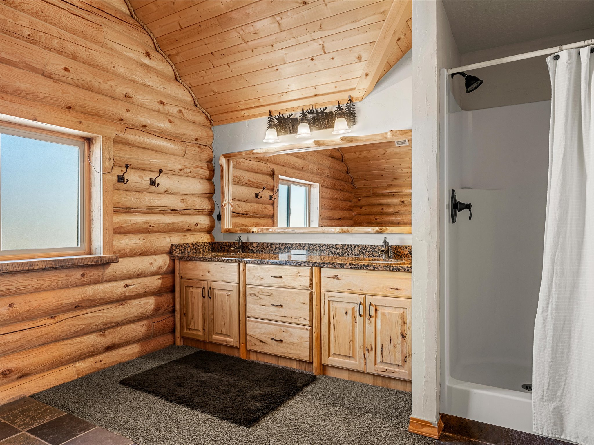 Full bath with a vaulted wood ceiling, double vanity, a shower stall, and log walls