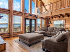 Living area with rustic walls, hardwood / wood-style floors, a water view, and a high wood ceiling