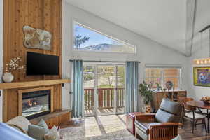 Living room with a glass covered fireplace, wood finished floors, healthy amount of natural light, and lofted ceiling