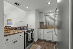 Kitchen with stainless steel appliances, white cabinetry, dark wood-type flooring, dark stone countertops, and tasteful backsplash