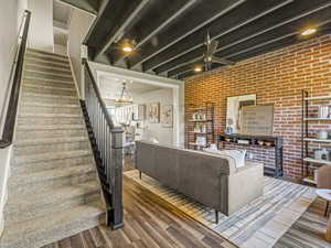 Living room with wood finished floors, brick wall, a chandelier, and ceiling fan