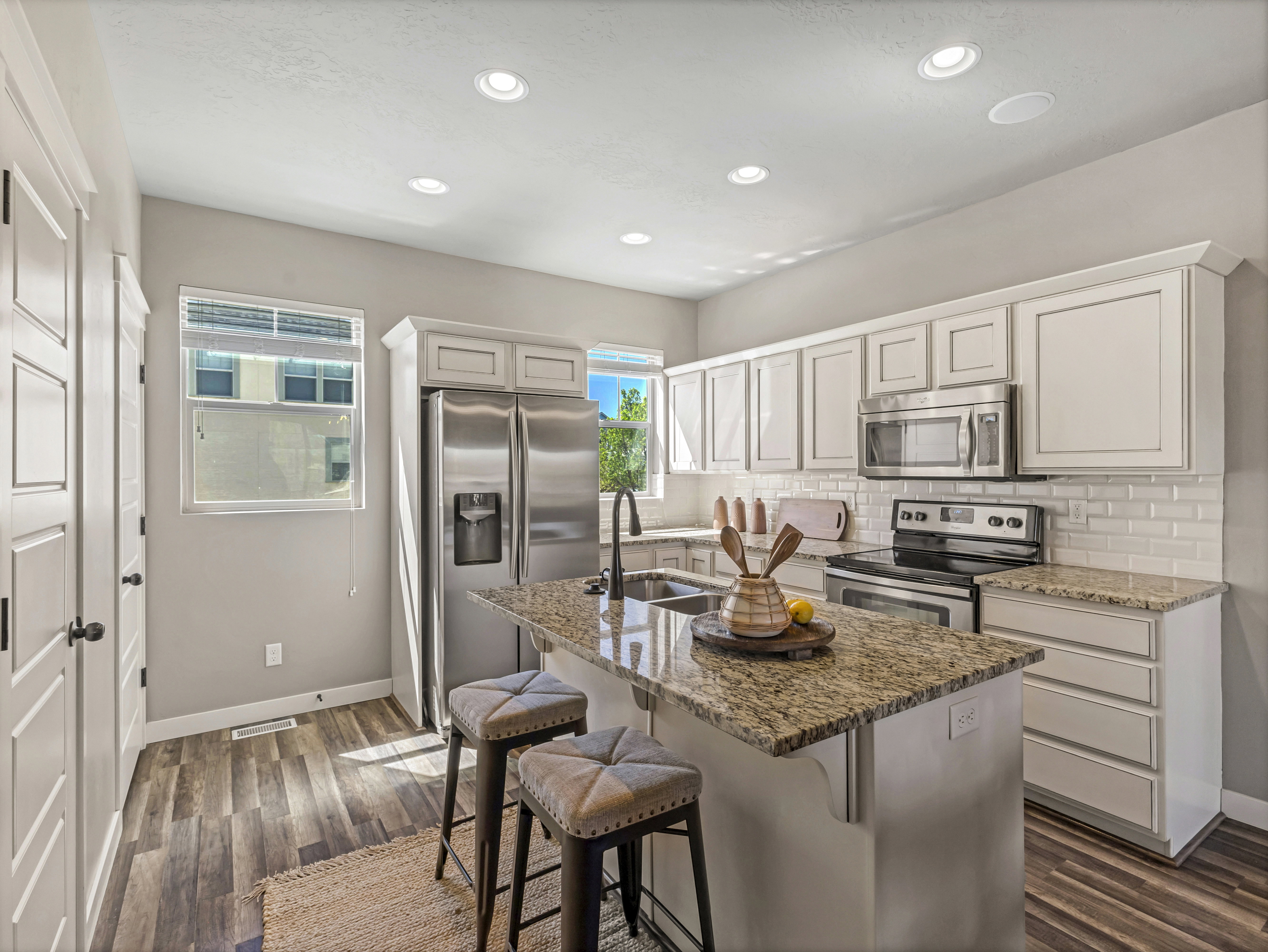 Kitchen with stainless steel appliances, a kitchen breakfast bar, light stone counters, tasteful backsplash, and white cabinets