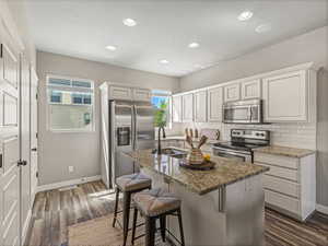 Kitchen with stainless steel appliances, a kitchen breakfast bar, light stone counters, tasteful backsplash, and white cabinets
