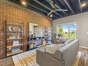 Living room with wood-type flooring, brick wall, beamed ceiling, and ceiling fan