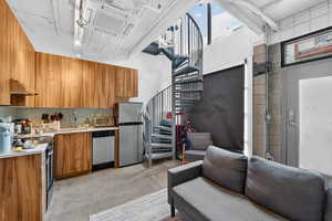 Kitchen featuring wood finish cabinetry, light countertops, concrete flooring, stainless steel appliances, and modern cabinets