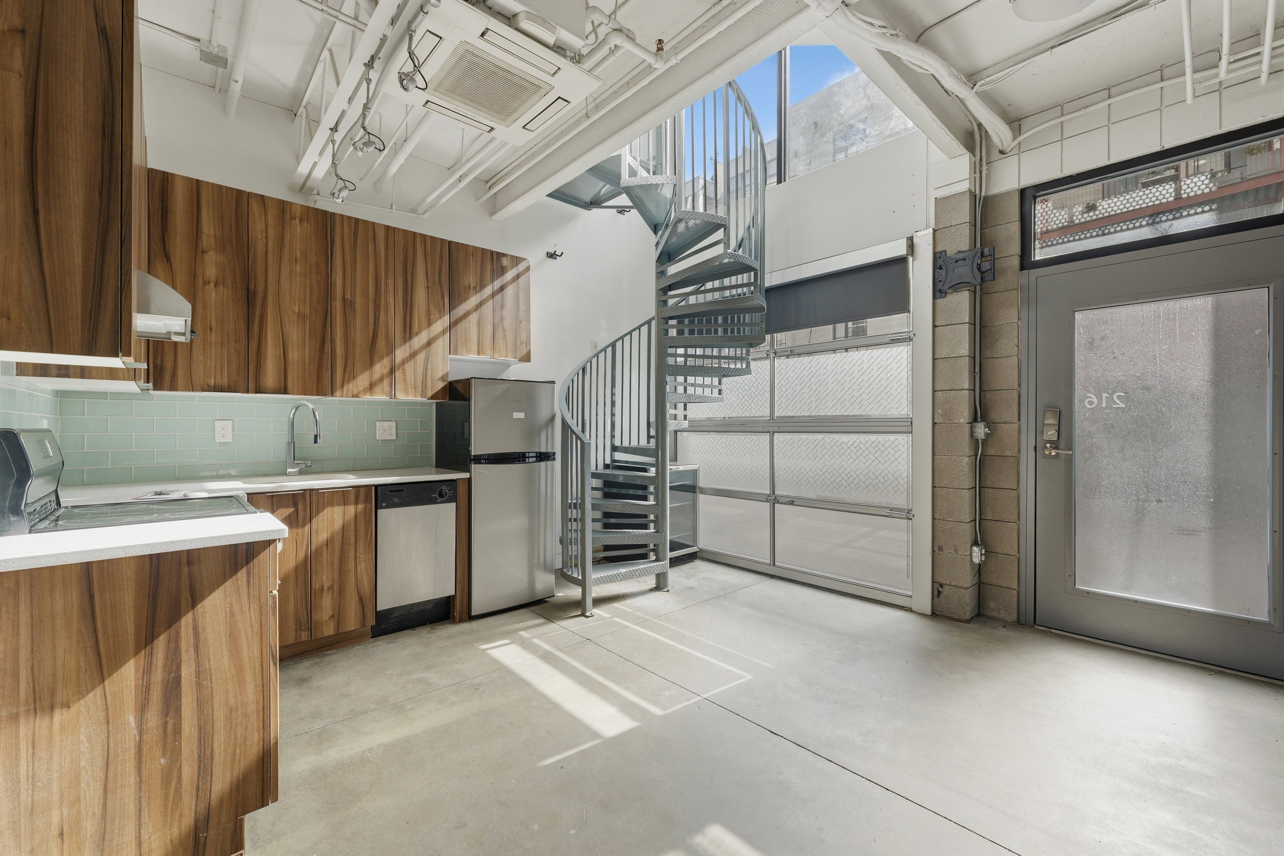 Contemporary kitchen with wood-finish cabinetry, light green subway tile backsplash, and stainless steel appliances