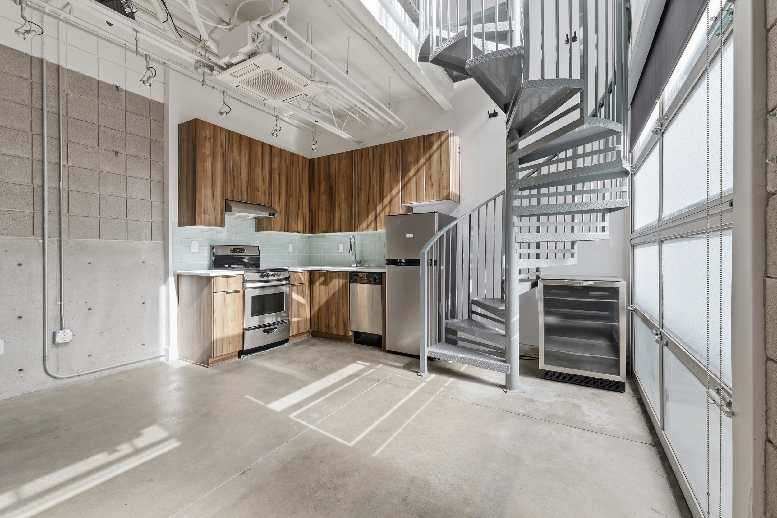 Industrial-style living space featuring a spiral staircase, concrete flooring, and exposed ceiling infrastructure