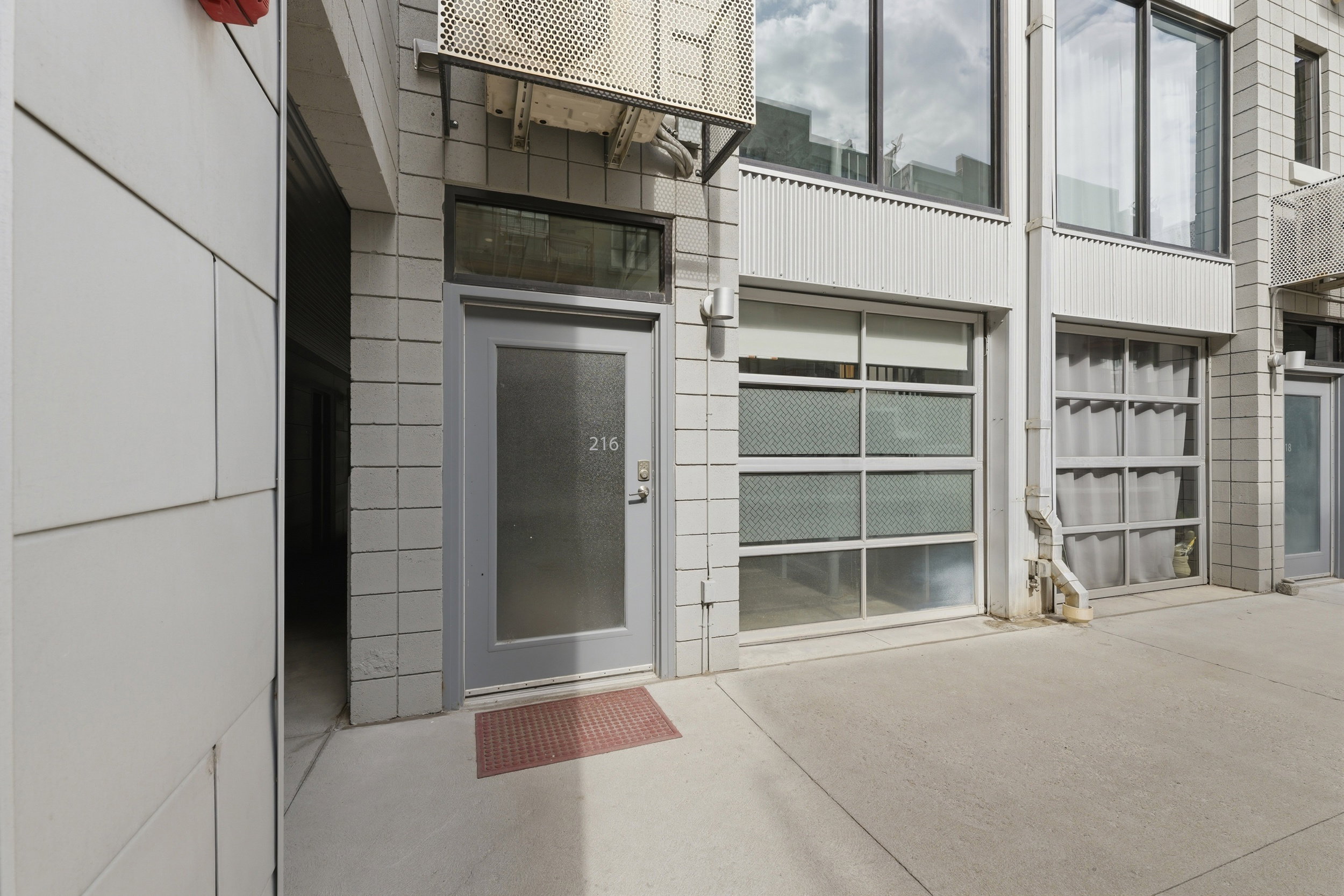 Modern facade featuring a gray entry door with frosted glass, industrial-style garage doors with multiple panes, and a textured block exterior