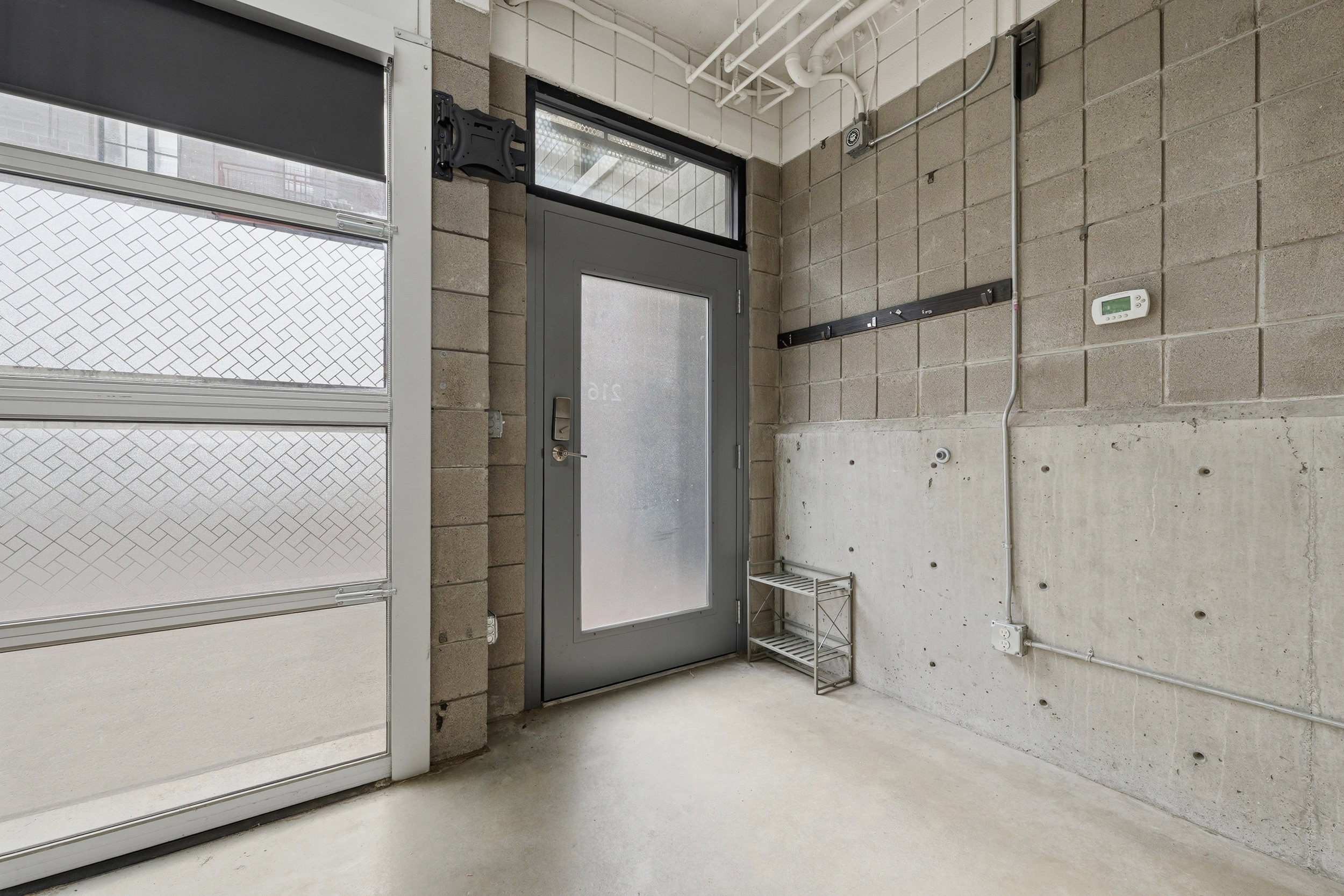 Entryway featuring a frosted glass panel door with transom window, concrete block walls, exposed conduit, and a polished concrete floor