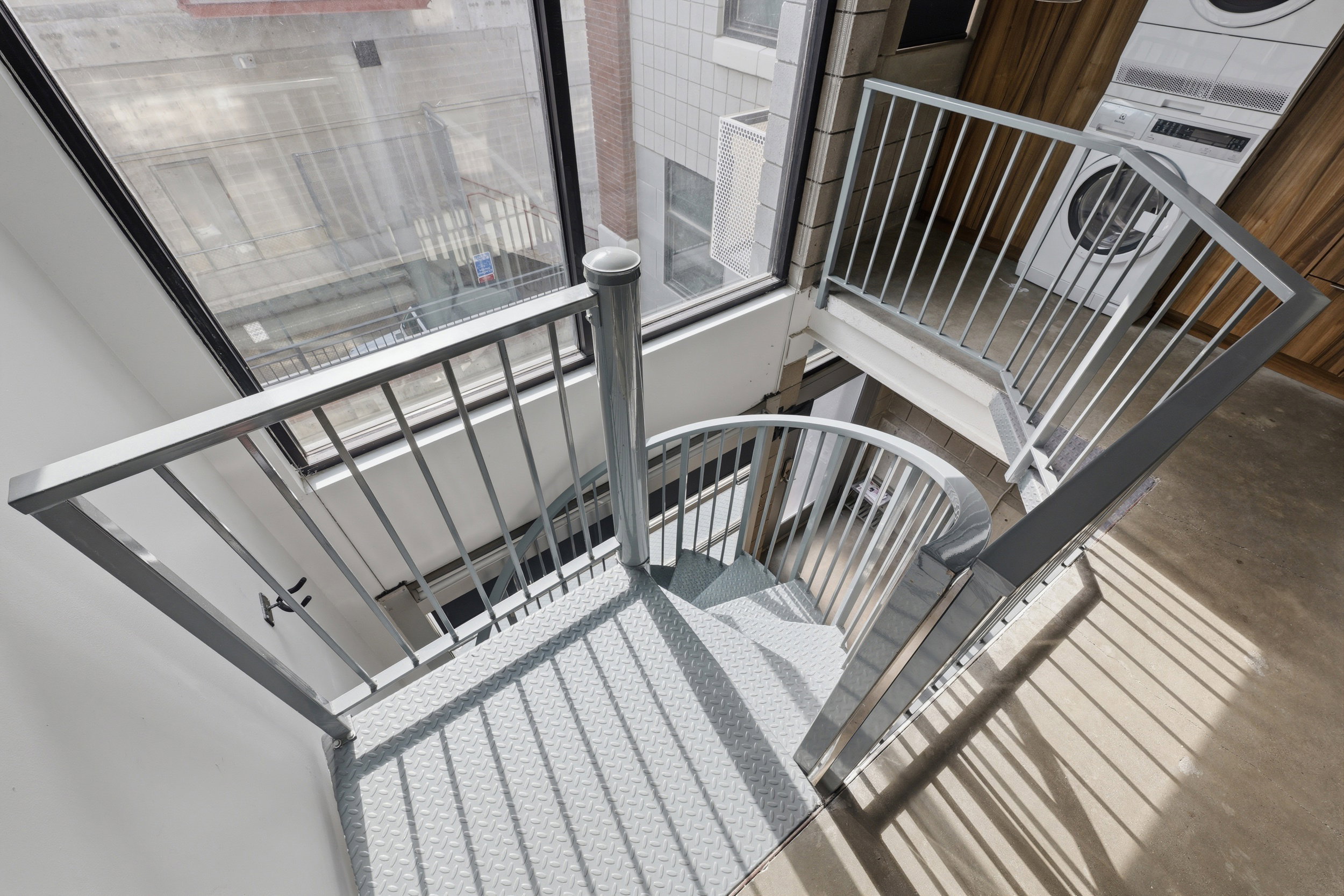 Spiral metal staircase with diamond-plate treads, metal railings, and a large multi-pane window