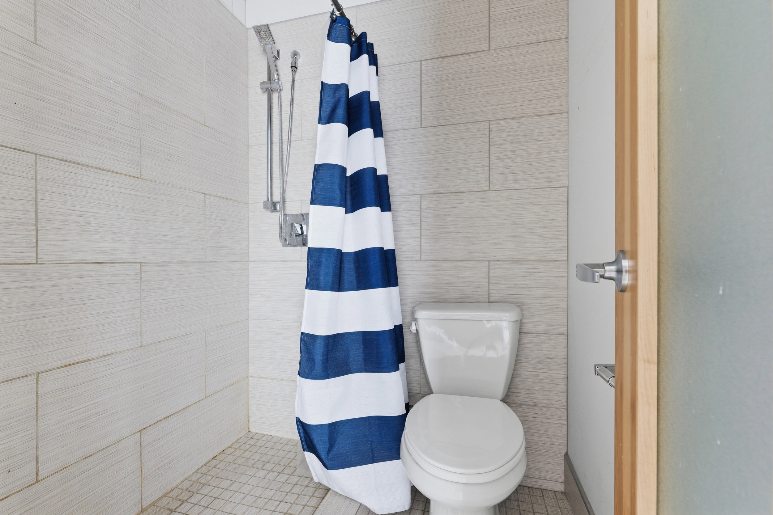 Shower stall featuring textured light-toned wall tiles, a mosaic tile floor, and a mounted shower system with a handheld sprayer