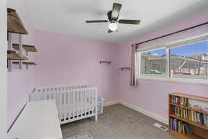 Bedroom featuring light colored carpet, a nursery area, and a ceiling fan