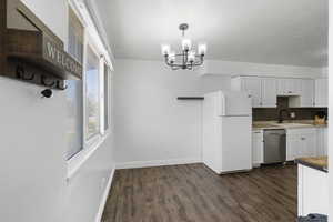 Kitchen with freestanding refrigerator, white cabinets, dishwasher, dark wood-style floors, and hanging lights