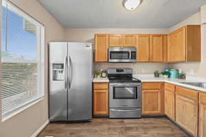 Kitchen featuring stainless steel appliances, light countertops, double basin sink, LVP flooring and wood finish cabinetry