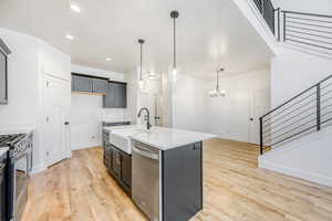 Kitchen featuring stainless steel appliances, light stone counters, an island with sink, light wood-style floors, and a chandelier