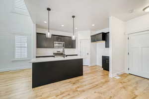 Kitchen with a kitchen island with sink, pendant lighting, light wood-style flooring, stainless steel appliances, and light stone countertops
