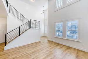 Unfurnished living room with a high ceiling, light wood finished floors, and a chandelier