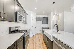 Kitchen featuring stainless steel appliances, light stone counters, light wood-style flooring, and pendant lighting