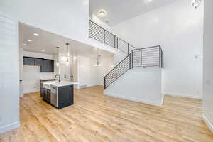 Kitchen featuring hanging lights, an island with sink, open floor plan, light wood-type flooring, and light stone countertops