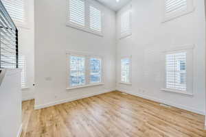Unfurnished living room featuring light wood-style flooring and a high ceiling