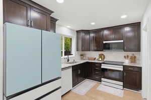 Kitchen with refrigerator, dark wood finish cabinetry, electric stove, light stone countertops, and recessed lighting
