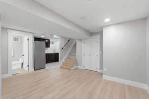 Finished below grade area with freestanding refrigerator, light wood-type flooring, and recessed lighting